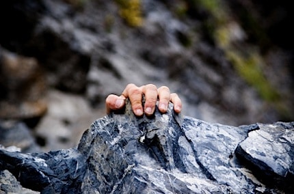 a man getting his hand on the rock above to scale the mountain